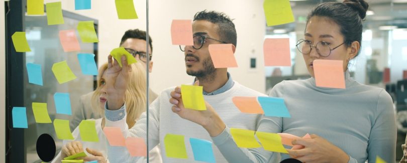 Team brainstorming ideas on a glass wall with sticky notes.