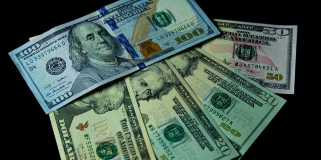 Detailed view of multiple US dollar bills against a black background, highlighting financial themes.