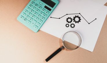 Calculator, magnifying glass, and chart with gears on paper.