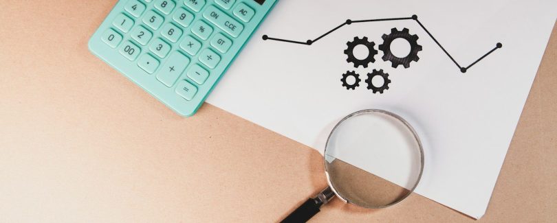 Calculator, magnifying glass, and chart with gears on paper.